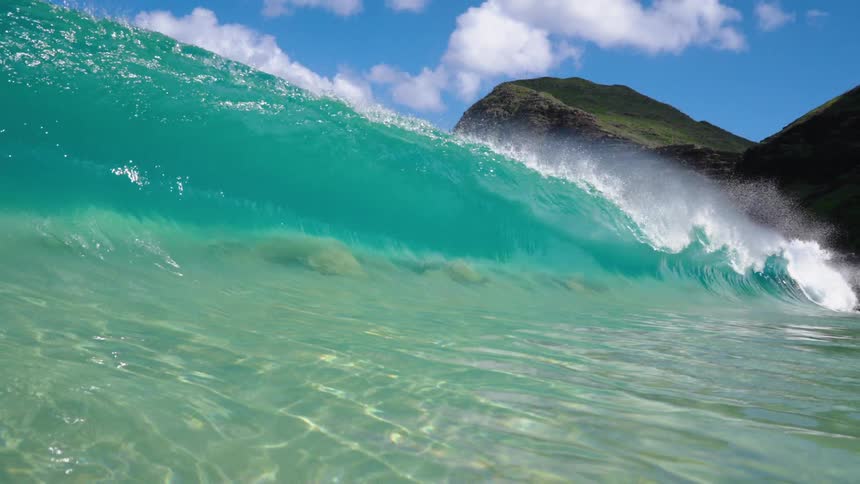 View of a sea wave breaking on a turquoise blue beach with the coastline beside it