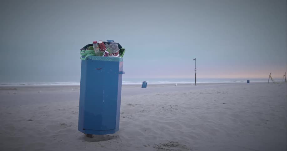 Overflowing trash bin amid the sand on the beach in the morning