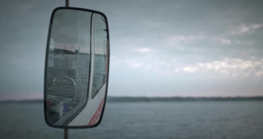 Side mirror reflects ocean waves and the side of the vehicle on an overcast day