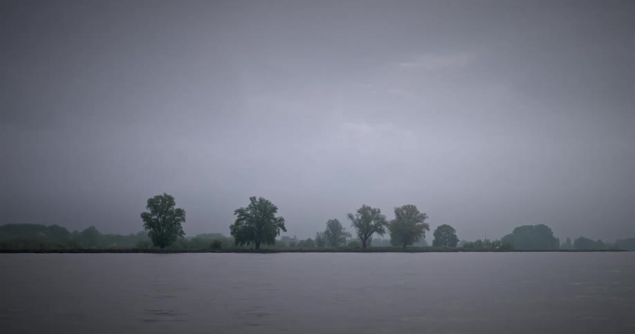 View of the river with a bank next to a grassland on a cloudy day
