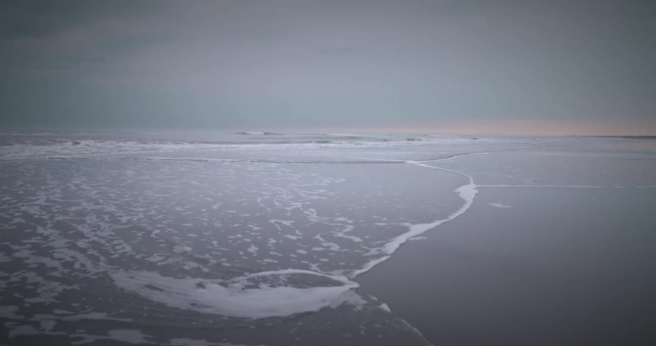 A sandy shore with low waves and cloudy sky