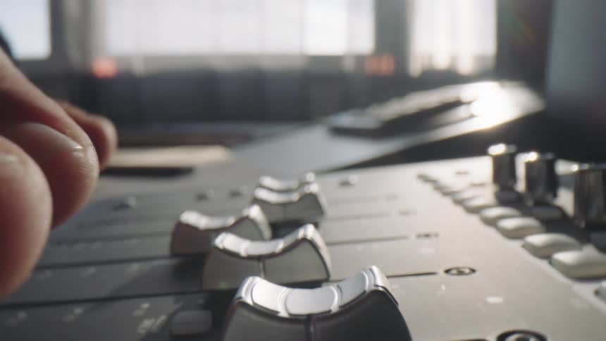 Man picks up a headset while seated in a studio at midday operating the digital mixer