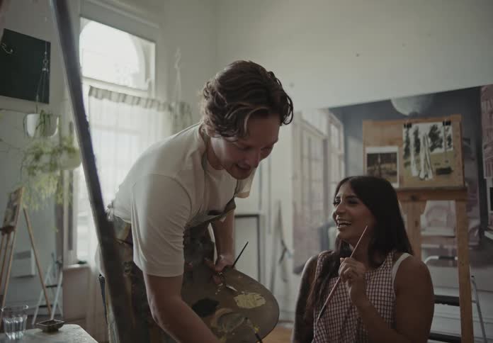 Man and woman talking and smiling while painting in a studio at midday