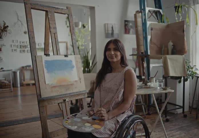 A woman on her wheelchair shows off her painting