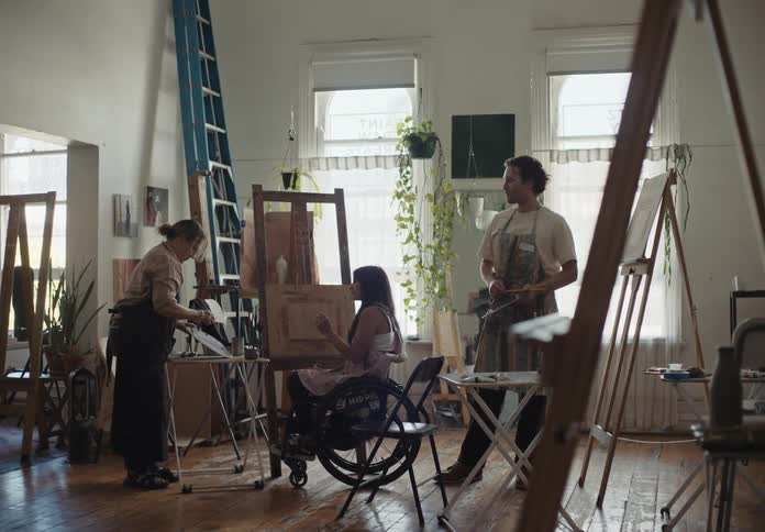 Woman teaching the palette with paint to two painters one of whom is in a wheelchair