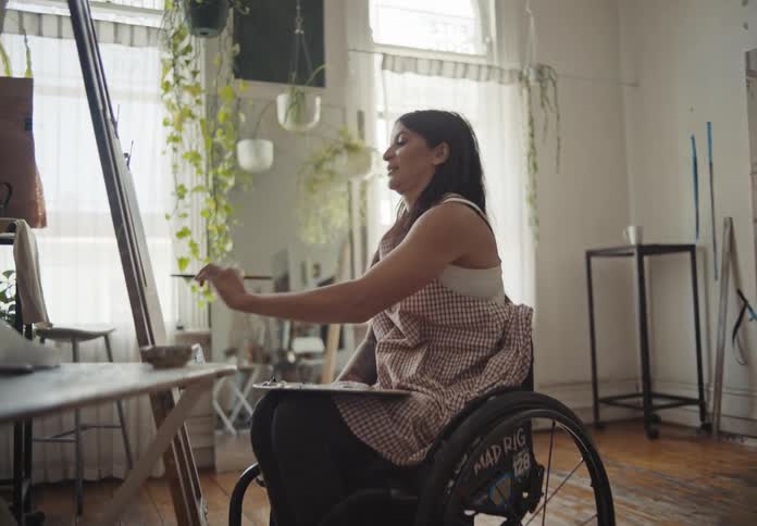 Female artist sitting in wheelchair paints while in art studio