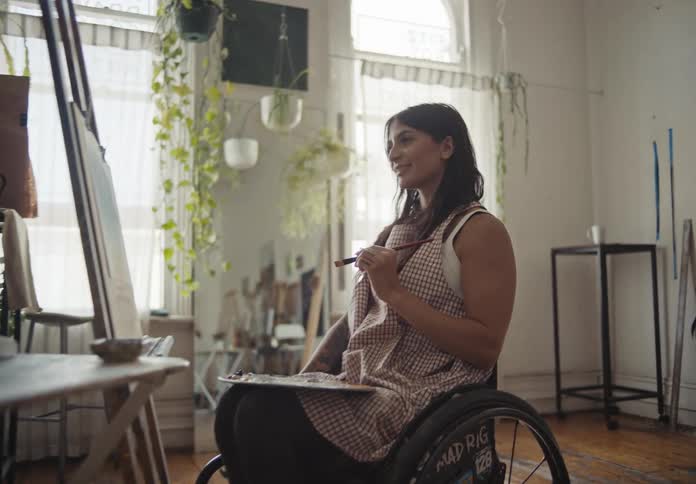 Woman in a wheelchair painting a smiling picture inside an indoor room
