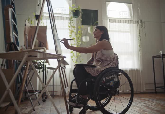 Woman in a wheelchair painting a picture in front of her
