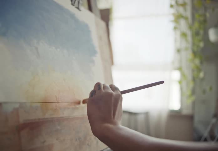 A woman is indoor painting on a canvas