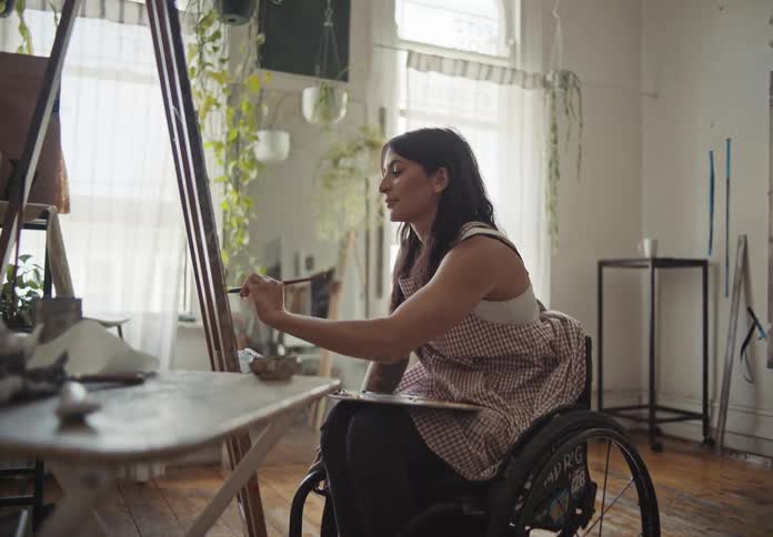 A woman in a wheelchair painting a canvas