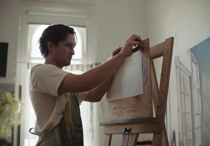 A young artist placing a sheet of paper on an easel