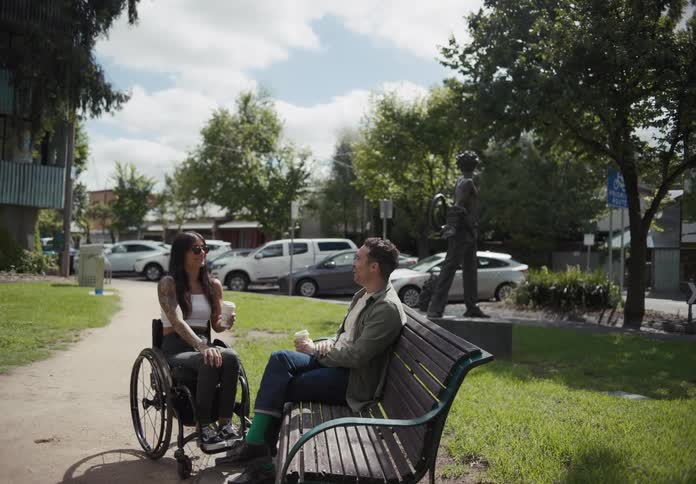 Lady in a wheel chair talking with a man seated on the bench outdoor at midday