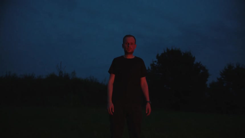 Man wearing black shirt stands outside at night trees in background