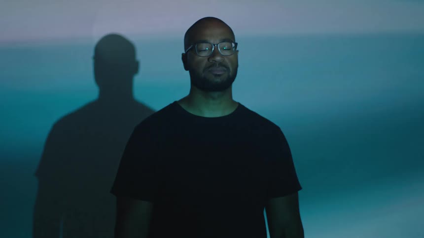 A man stand behind a wall indoor with lights flashing on his face