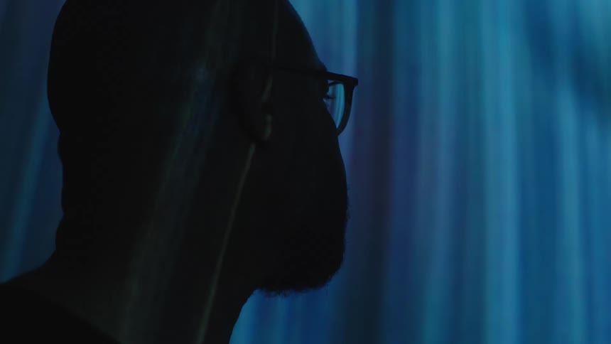 Closeup of the side of a mans face with an image being projected on a wall in a dark room