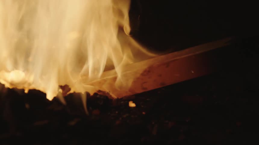 Closeup of a piece of wood being placed in the middle of a ground fire at night