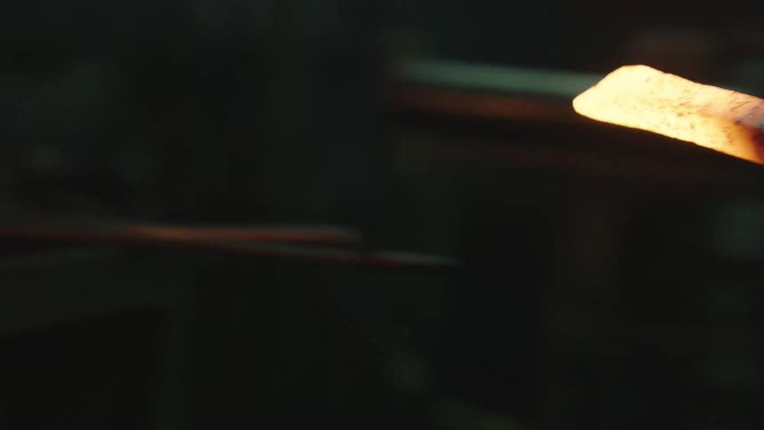 A person heating up a rod in a fire and hammering the hot rod