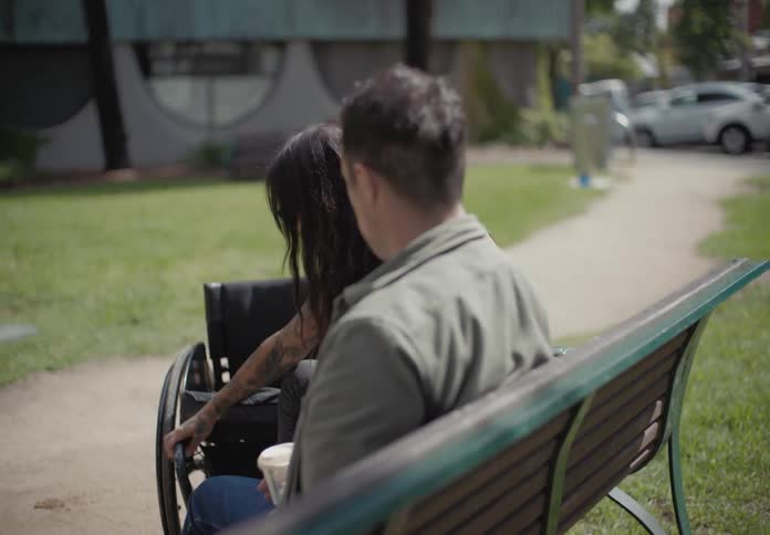 Woman in a wheelchair handing her phone to her colleague and sitting alone on the adjacent bench