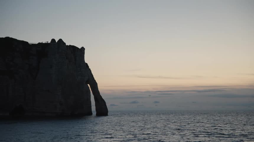 A large rock island with people standing on the top in the ocean