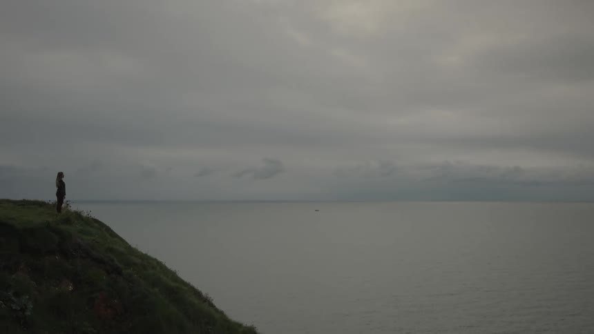 Woman on a hill facing the sea on a cloudy day