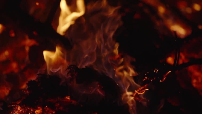 Flames rise and embers glow as a campfire burns at night
