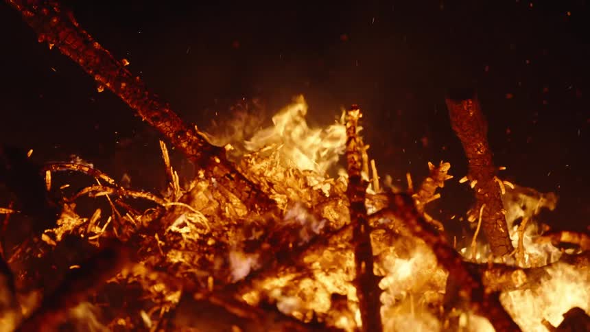 Closeup of fire catching on branches at night in slow motion