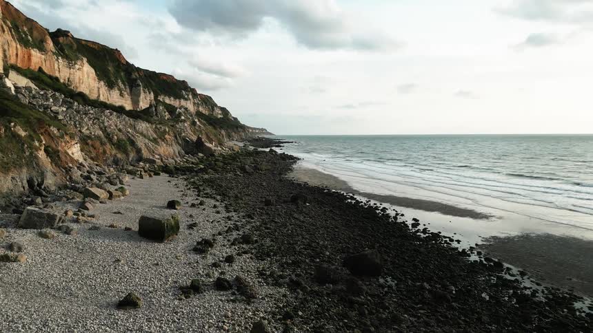 Waves rolling onto beach at base of cliffs reflect sunlight