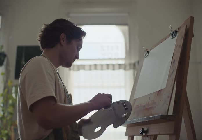An artist mixing oils on a palette prepares to paint in his studio