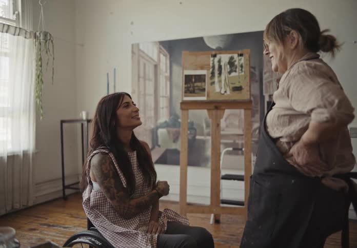 Two women talking indoor while looking at a painting on the wall