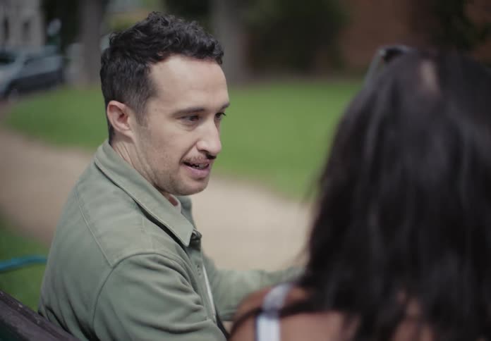 Portrait of a man sitting next to a woman on an outdoor bench talking and showing something on his phone to her