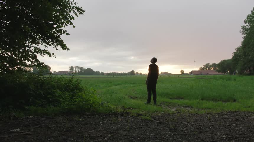 A man in a field in a rural town admiring the sunset