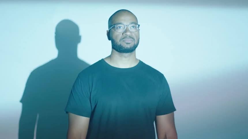 A black man wearing a black shirt and glasses as light shine on his face