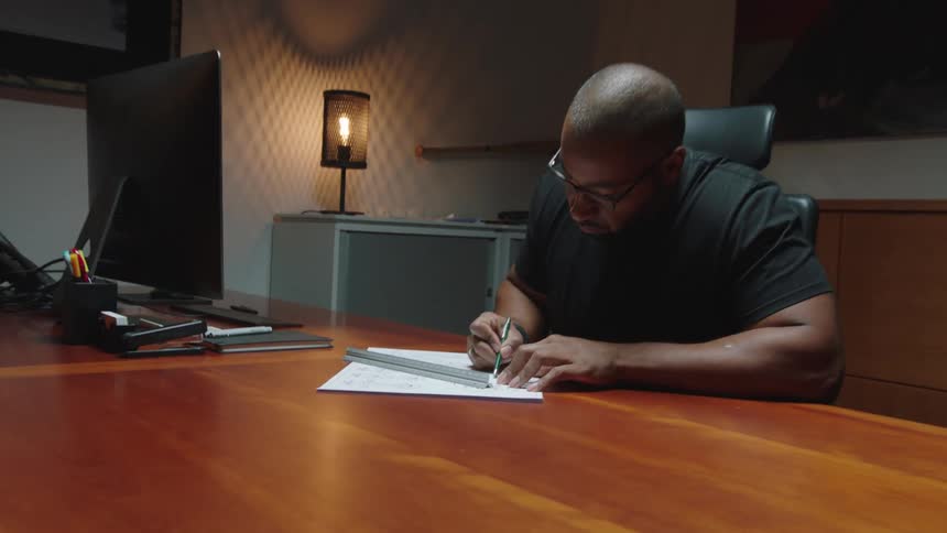 A person writing on a paper at a desk with a computer monitor and office supplies