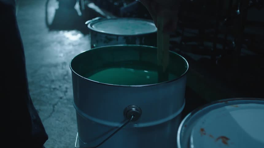 A person mixing paint inside a metallic bucket