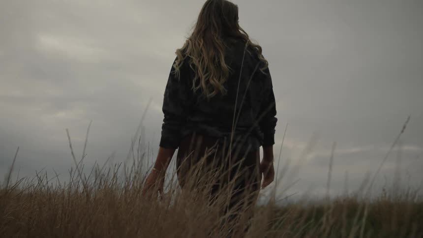 Silhouette of a woman walking on a grass field under a gray sky