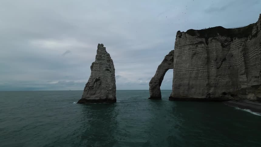 Aerial view of a large cliff and a broken off rock formation over the ocean