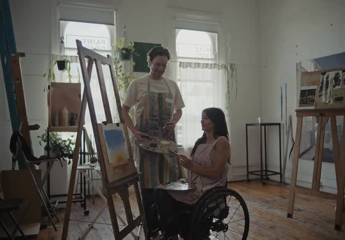 A woman paints a picture while talking to a man