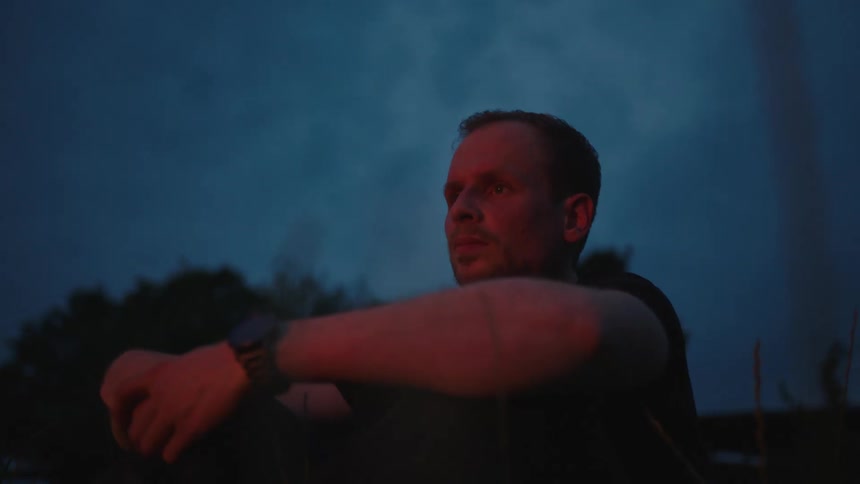 Man sitting on the grass with the reflection of a campfire at night