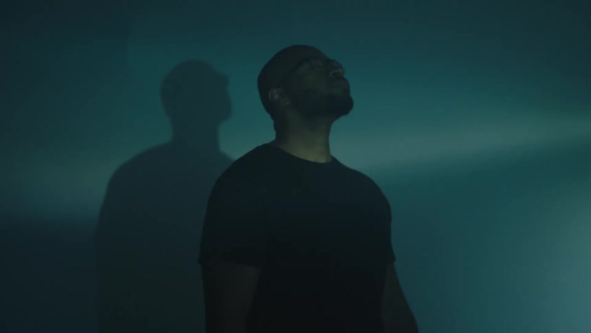 A man is standing still and receiving beams of light and his shadow forms on the wall
