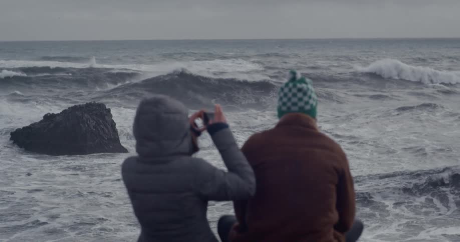 Two people sitting a watching ocean waves roll in on cloudy day
