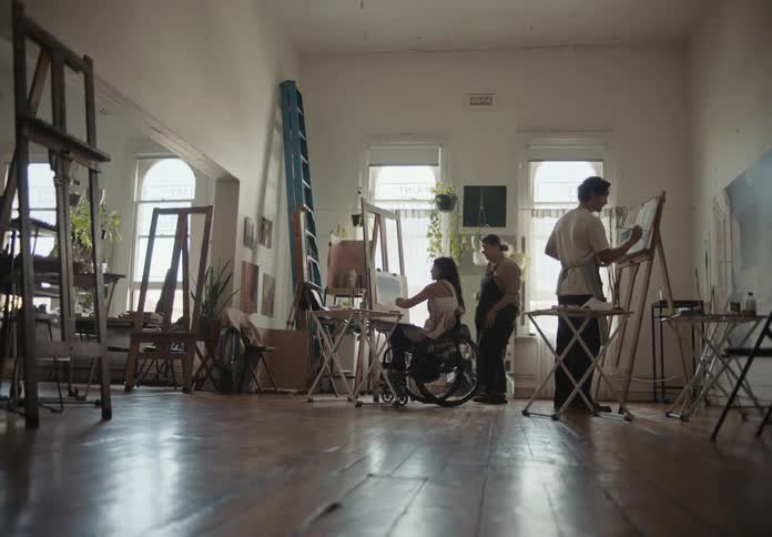 People painting in an art studio with various art supplies and paintings around them