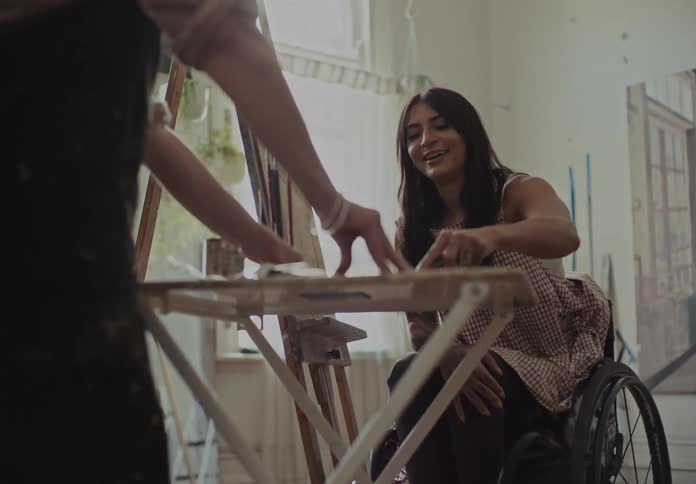 Woman assisting a person in a wheelchair with painting in an indoor room