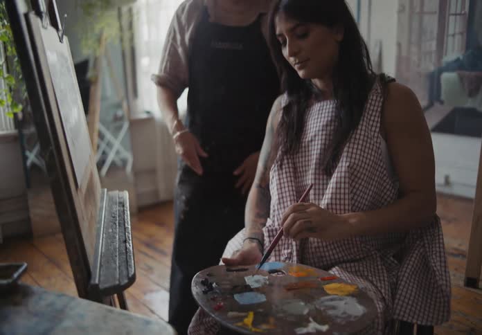 A lady painting indoor while getting instructions from an older woman