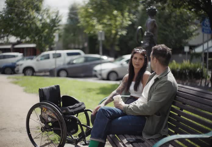 Man and woman sitting on an outdoor bench chatting and having coffee