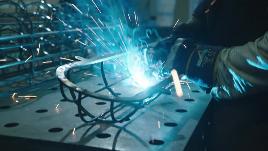 A person in protective gear welding a metal grid in an industrial setting