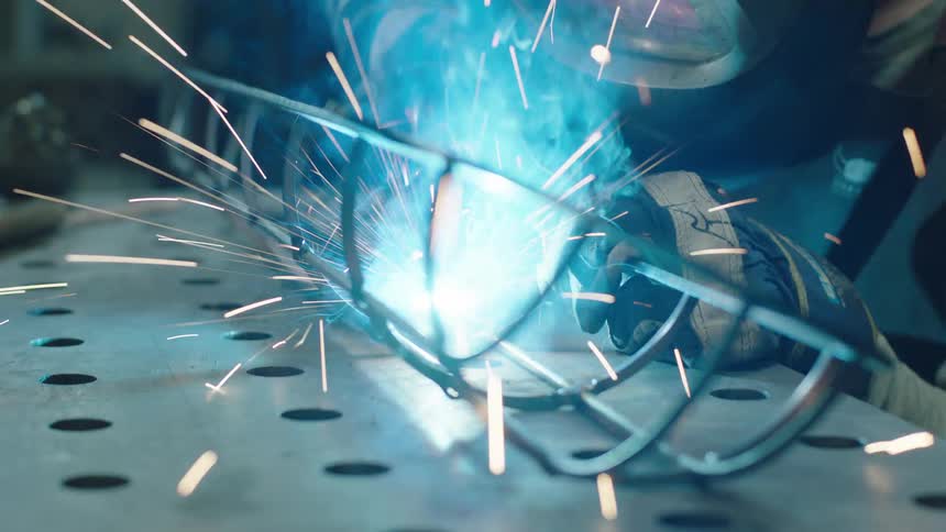 A person in protective gear welding a metal grid in an industrial setting