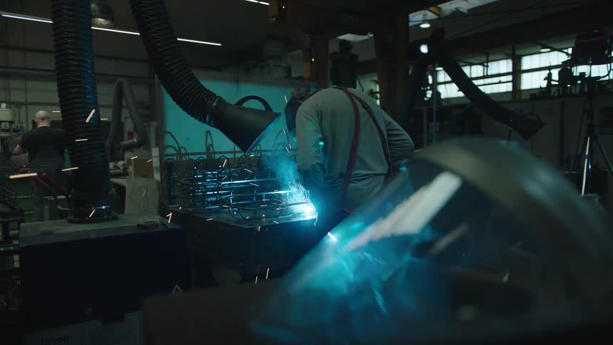 A person with his back is welding something that is making a lot of blue spark