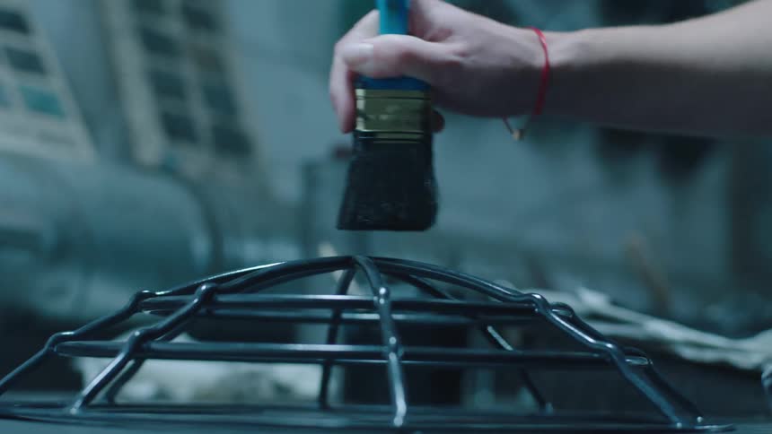 Closeup of a womans hand passing a brush over a metal rod