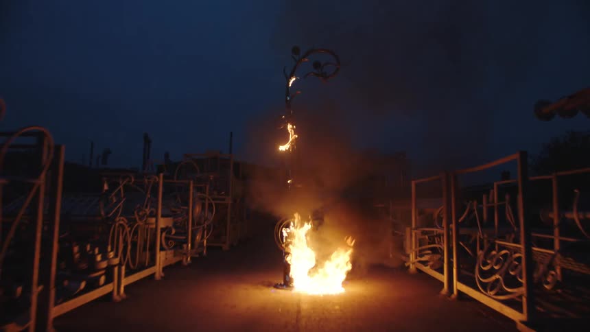 A structure is on fire surrounded by machinery and equipment in the dark