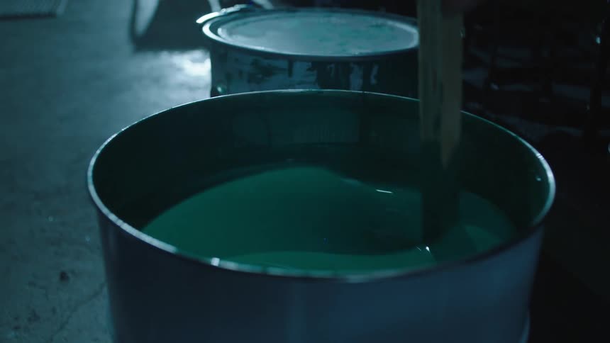 Someone using a wooden tool to stir a liquid inside a blue barrel